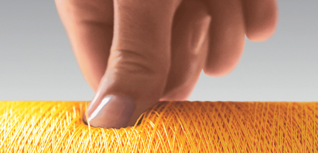 Thumb pressing on a yellow spool to show how soft the spool ist wound