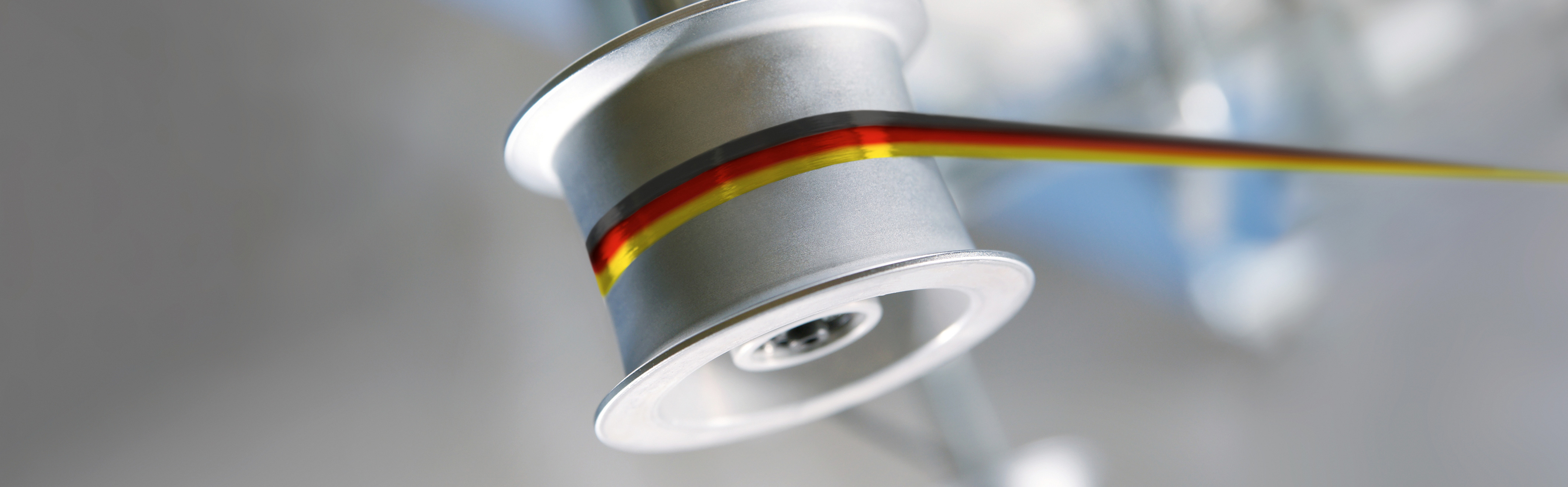 Rolle - Teil einer SAHM Spulmaschine Rolle mit schwarz-rot-goldenem Bändchen - Detailfoto einer SAHM Spulmaschine