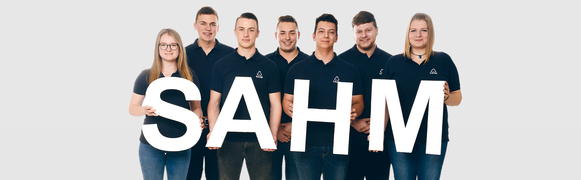 SAHM Auszubildende Sieben SAHM Auszubildende, die vier Buchstaben "SAHM" vor sich halten